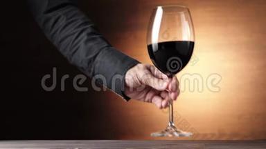 豪华红酒。 手拿着一个酒杯，在棕色背景下从桌子上拿出美味的葡萄酒。 玫瑰酒